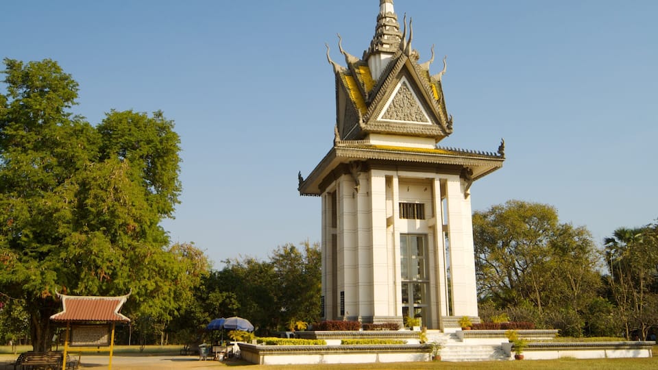 A traditional Thai temple with a tiered roof, surrounded by lush greenery and a small pavilion with a tiled roof.