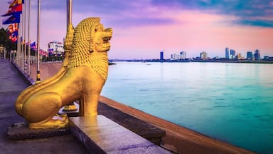 Una estatua dorada de un león junto a la orilla, con el horizonte de una ciudad al fondo.