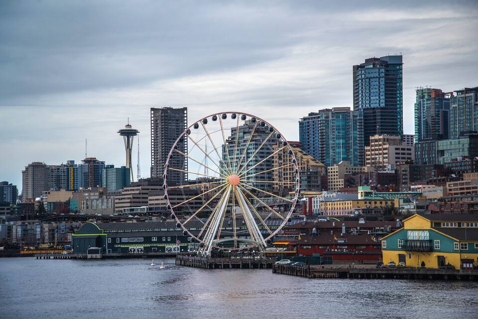 A large Ferris wheel in a cityscape with tall buildings and a waterfront.