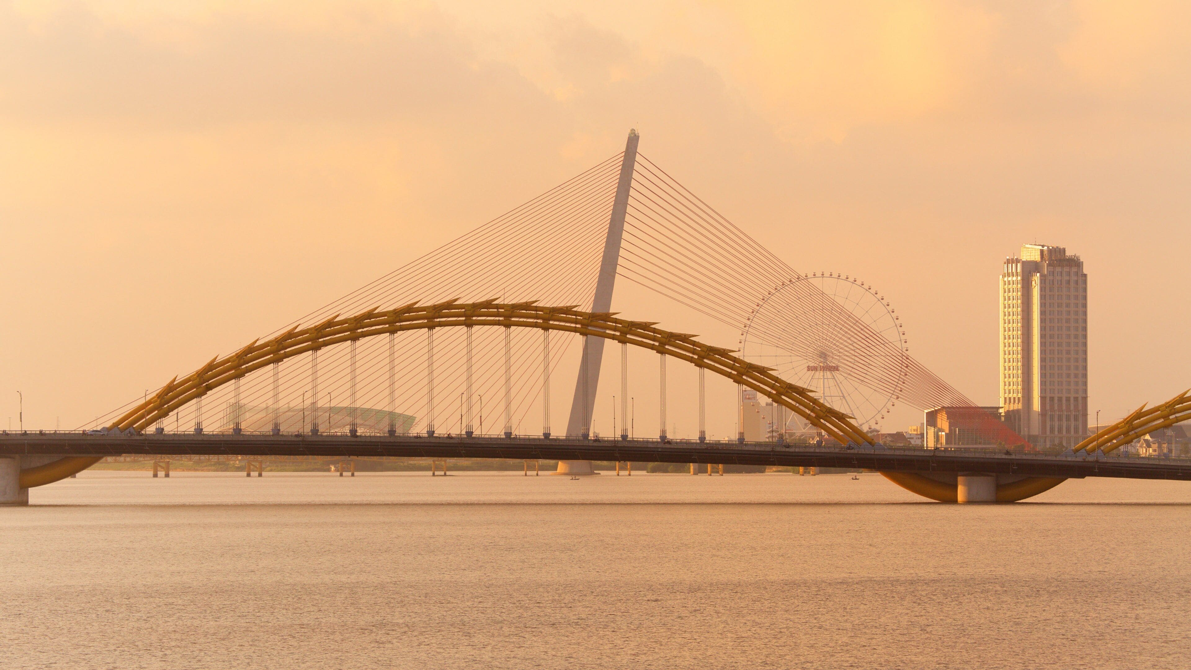 A bridge with a distinctive arch design over a body of water, with a tall building in the background.