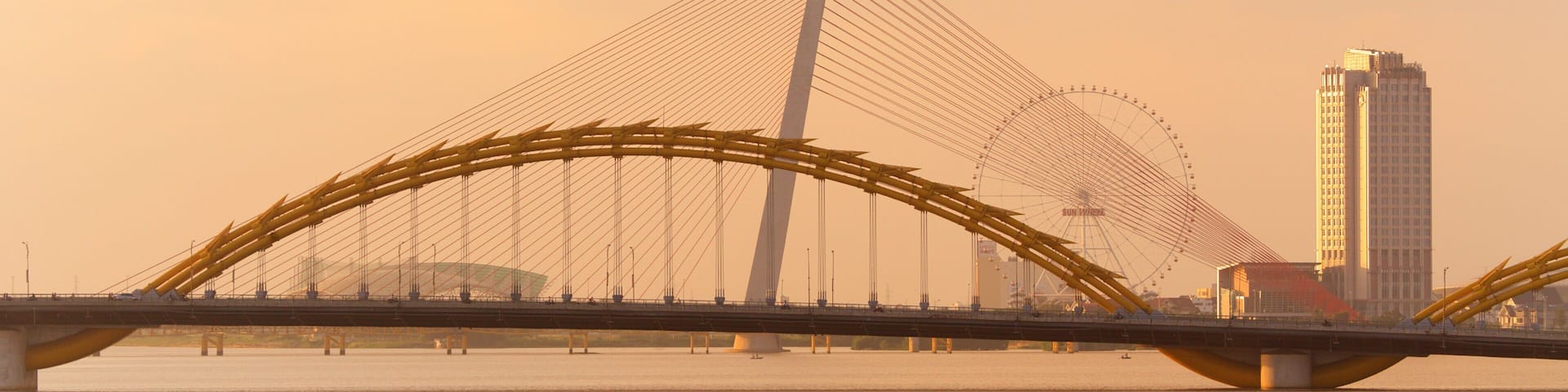 A bridge with a distinctive arch design over a body of water, with a tall building in the background.