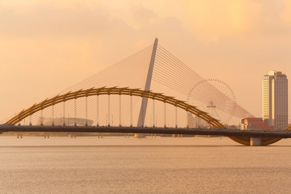 Un pont doté d’une arche au design particulier, enjambant une étendue d’eau, avec un grand immeuble en arrière-plan.