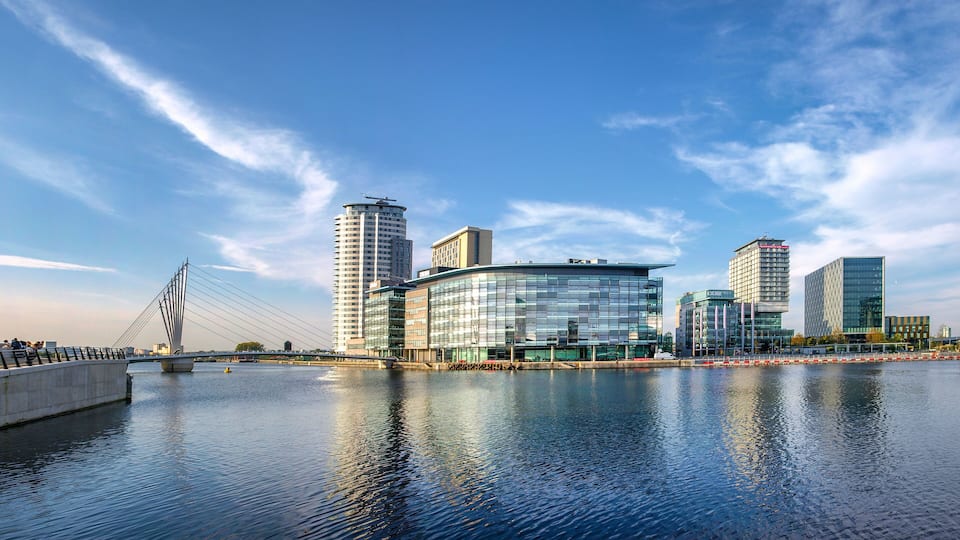 A modern cityscape with a river, a cable-stayed bridge, and contemporary buildings.