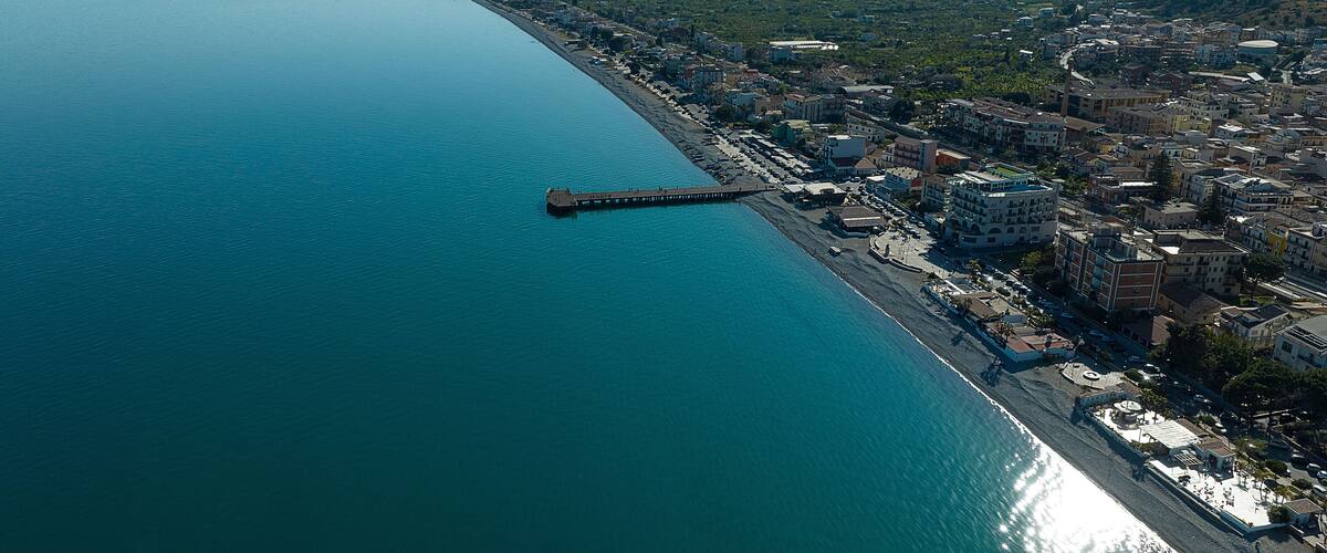 A coastal city with a pier extending into the sea, surrounded by buildings and greenery.