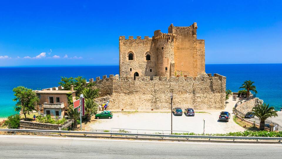 A historic stone castle by the sea with a clear blue sky.