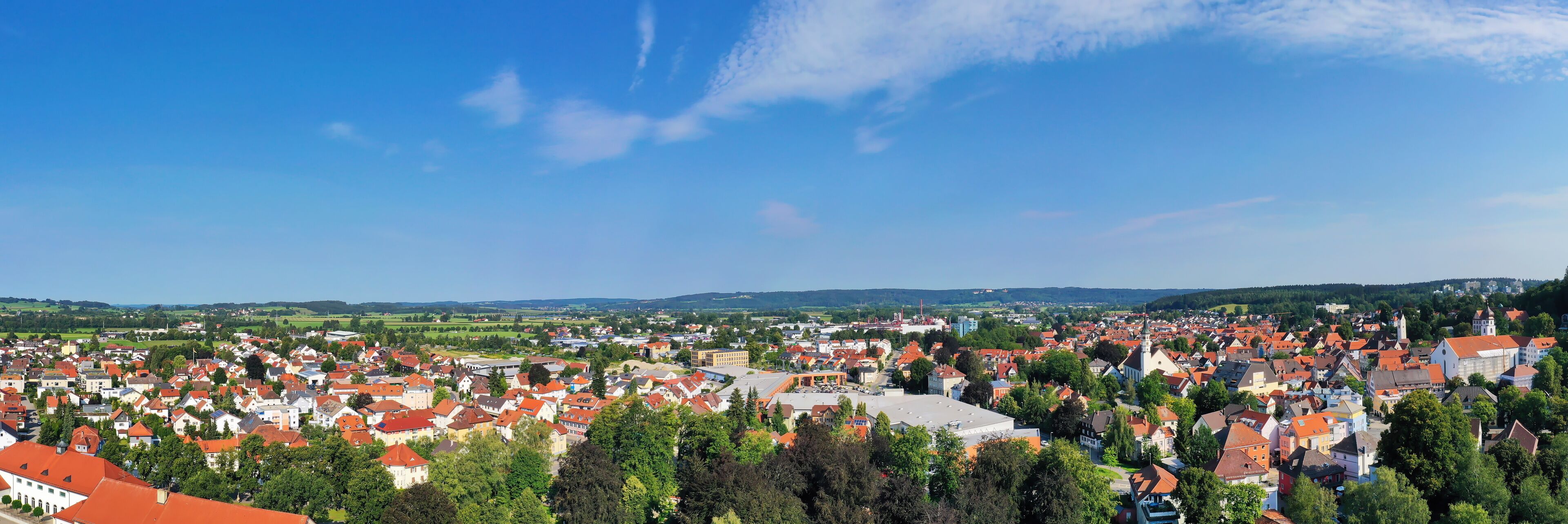 A town with red-roofed buildings, green hills, and a clear blue sky.