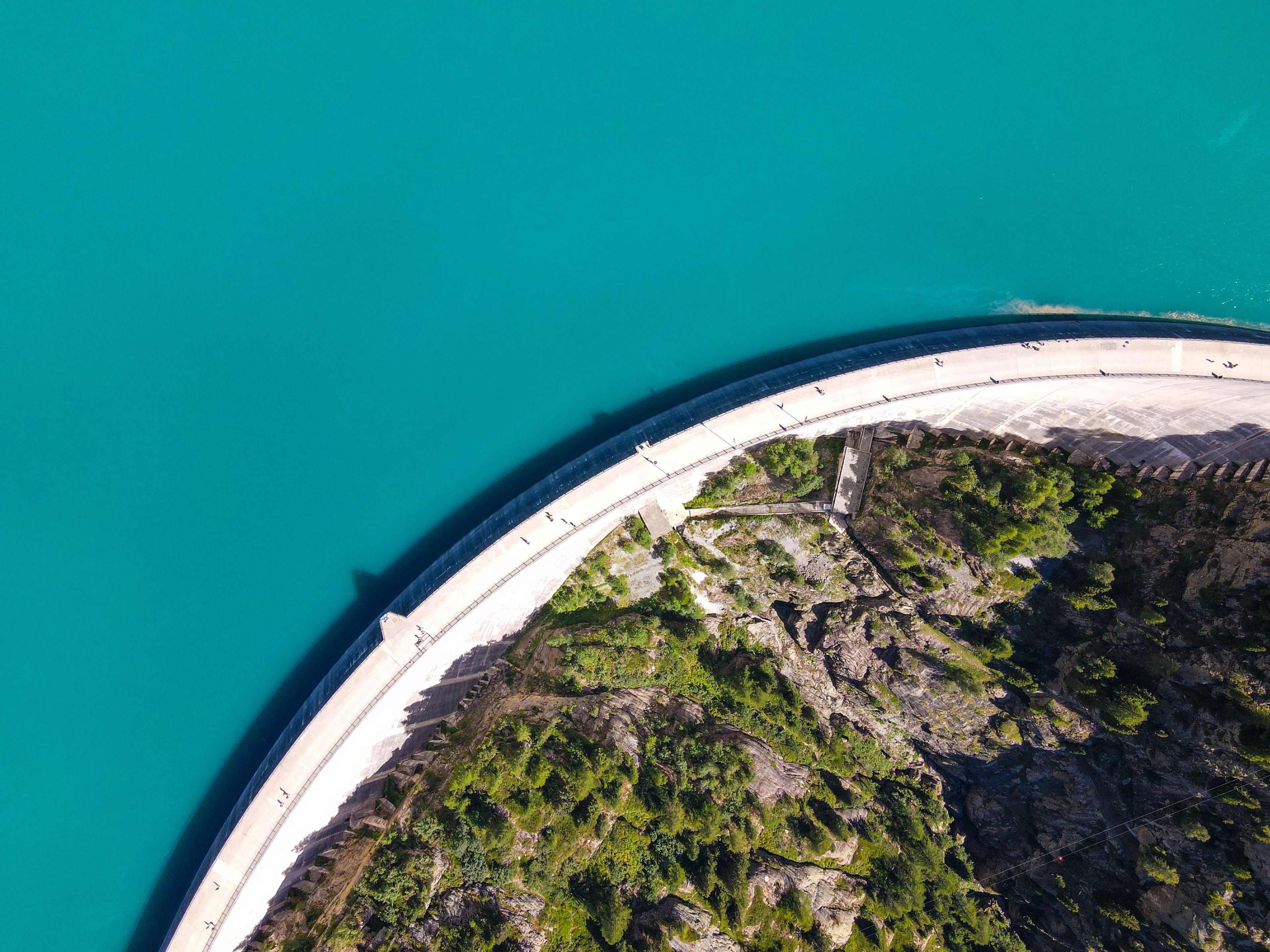 Vue aérienne d’une zone côtière avec une grande structure en béton, qui pourrait être un barrage ou une digue, et un littoral rocheux à la végétation clairsemée.