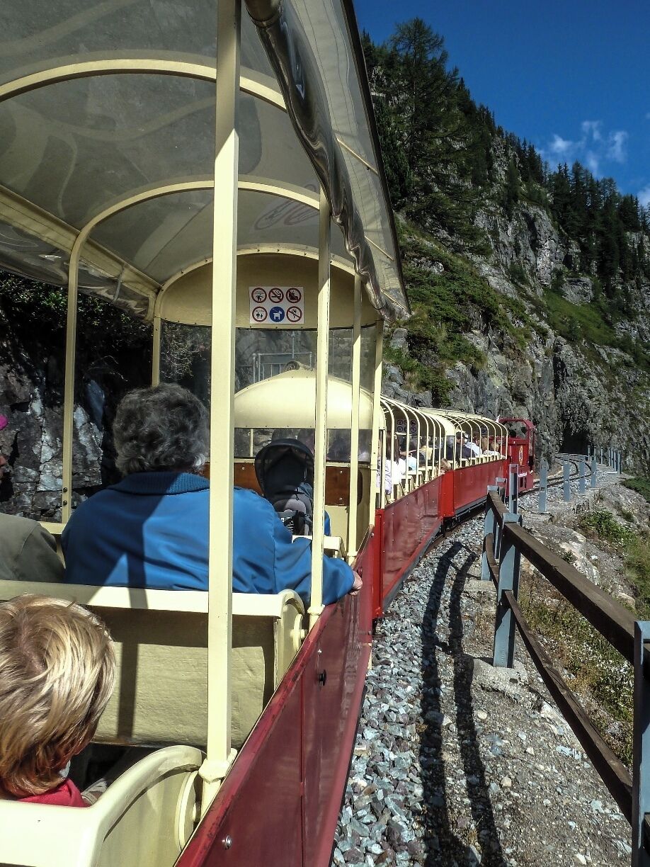 A small red train with passengers traveling along a rocky mountain track.