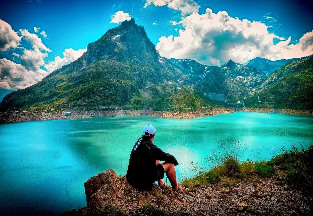 A person sitting on a rock overlooking a turquoise lake with mountains in the background.