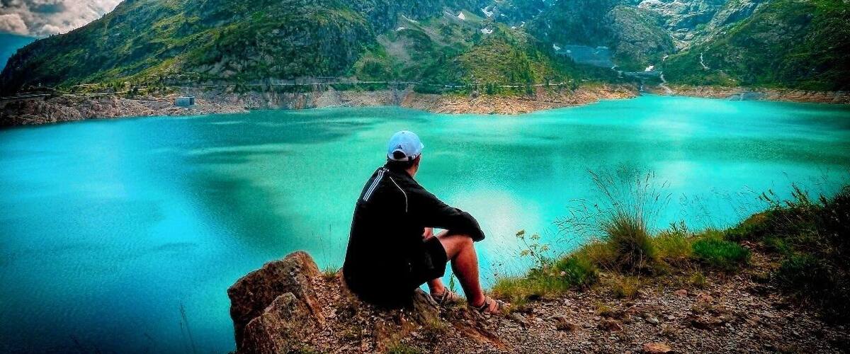 A person sitting on a rock overlooking a turquoise lake with mountains in the background.