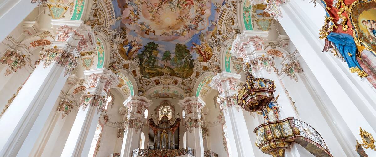 An ornate church interior with elaborate frescoes, gilded decorations, and a large organ.