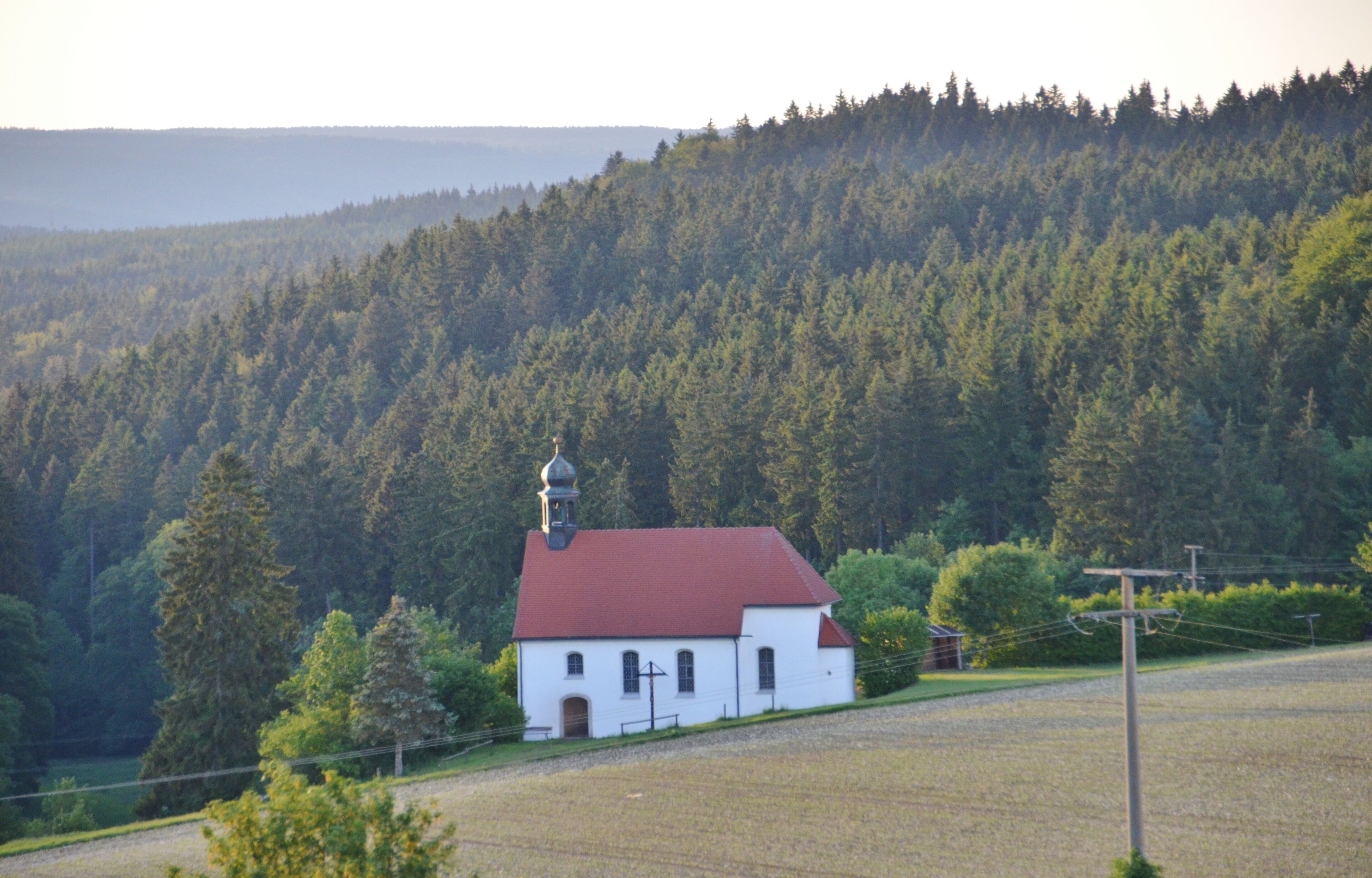 A white church with a red roof surrounded by a forested hillside.