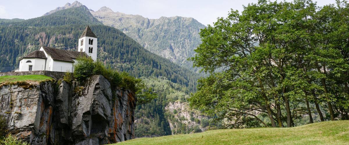 A white church on a cliff with a mountain backdrop.