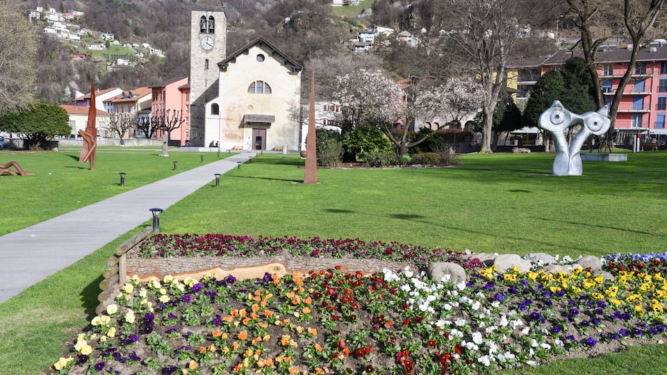 A park with a flower garden, a church, and a mountain in the background.