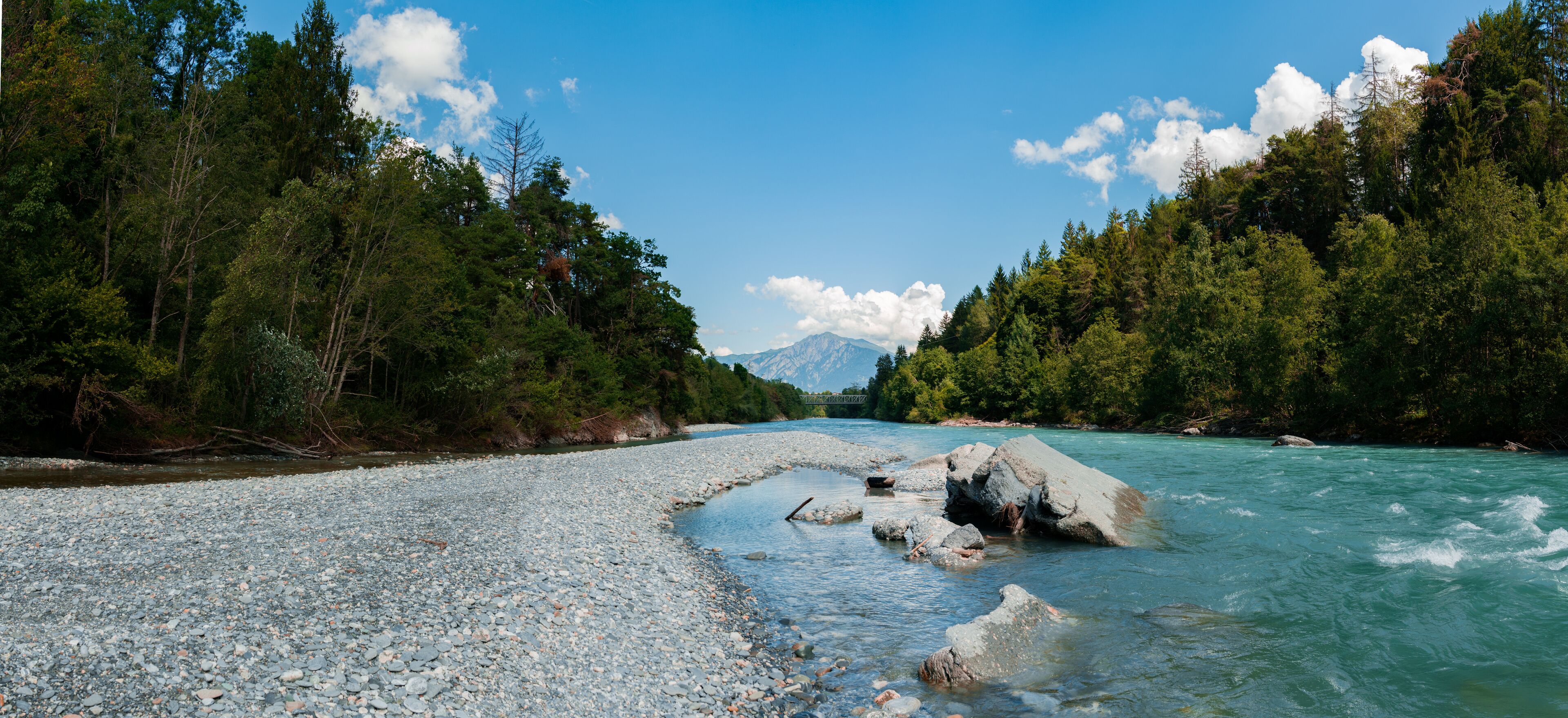 A river with clear water, surrounded by dense green forest and rocky banks.