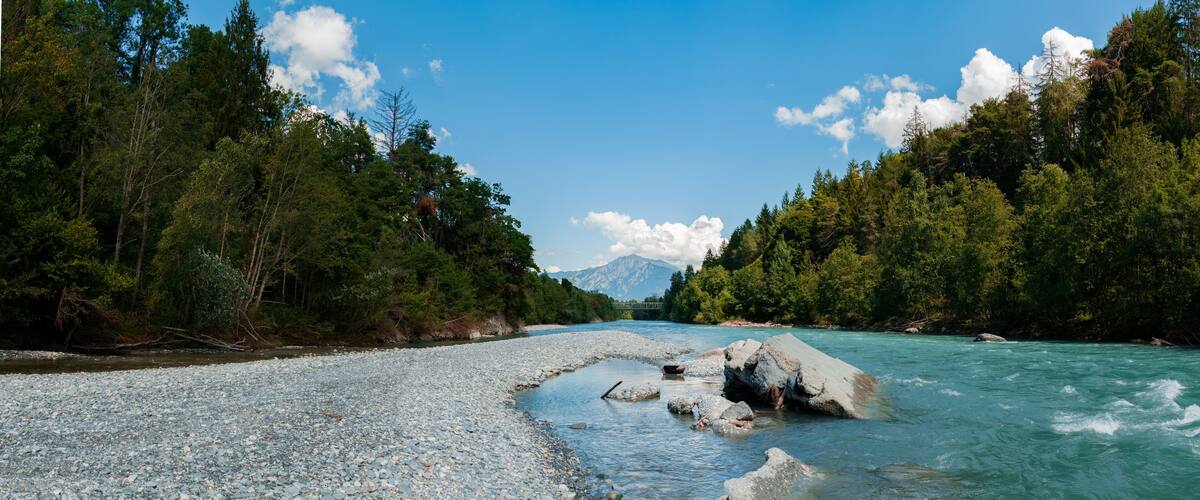 A river with clear water, surrounded by dense green forest and rocky banks.