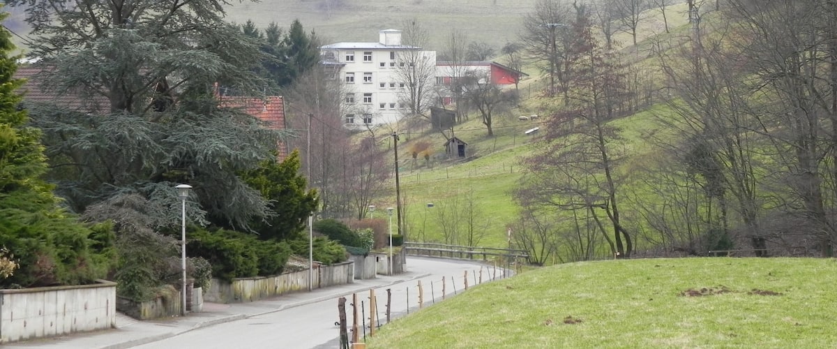 A rural landscape with a road, a white building, and a red-roofed structure in the distance.