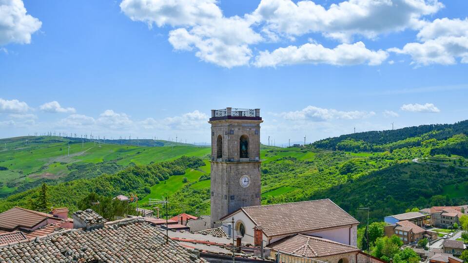 A historic tower with a clock, surrounded by terraced houses and lush green hills.