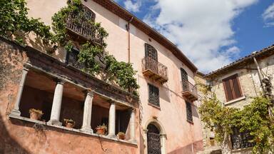 Un edificio storico con facciata rosa, un balcone con piante e una scala che conduce all'ingresso.