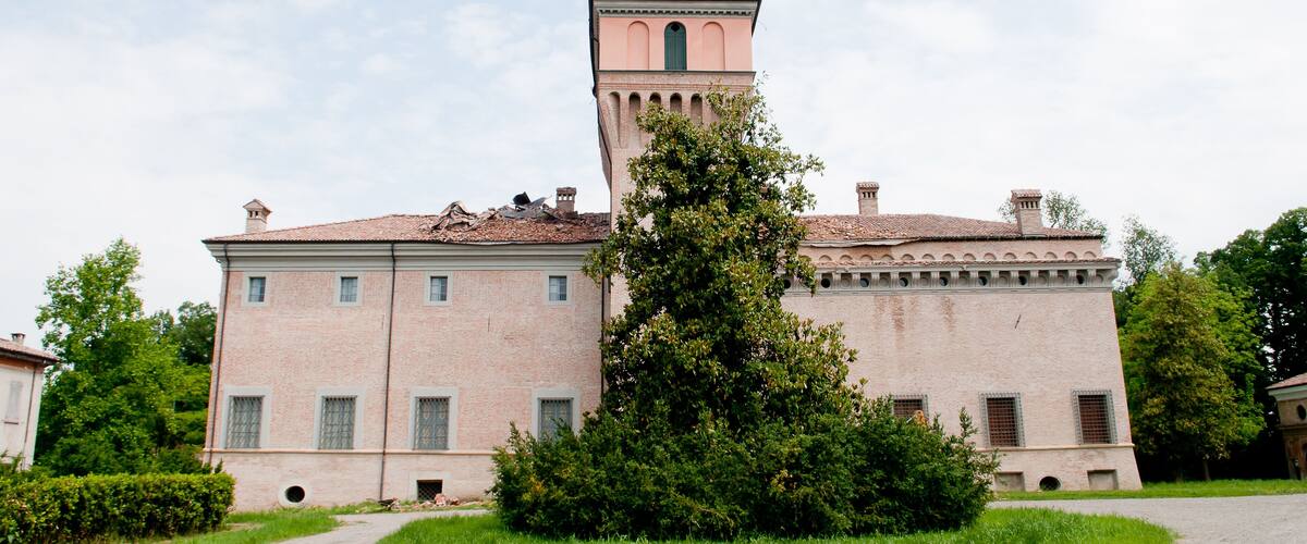 A large pink building with a tower, surrounded by greenery and a clear sky.