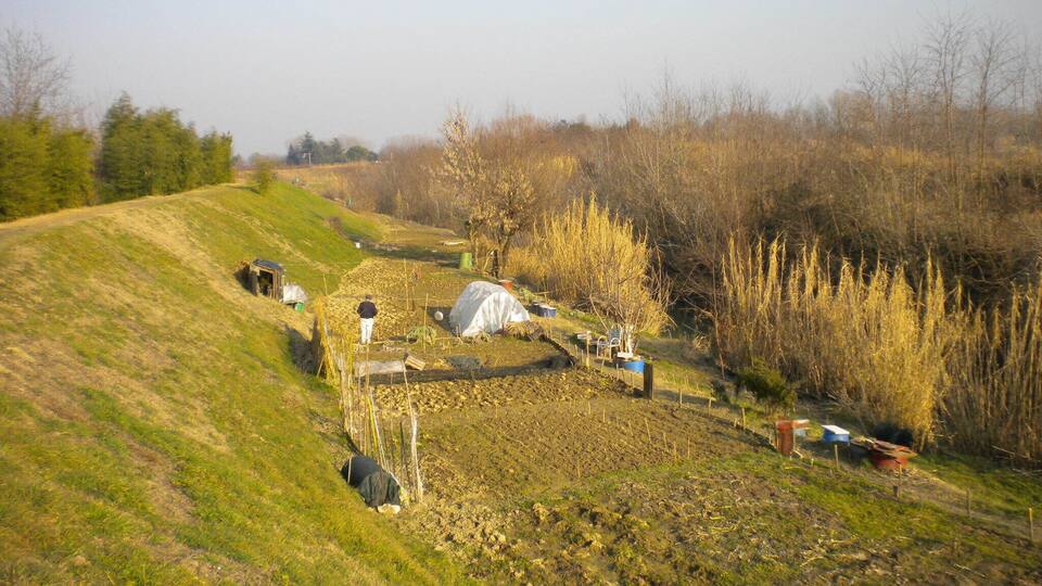 A rural landscape with a sloped field, a person walking, and a covered structure.