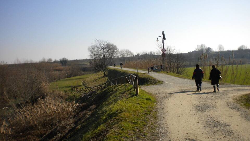 A rural dirt road with a metal guardrail, a cyclist, and two pedestrians.