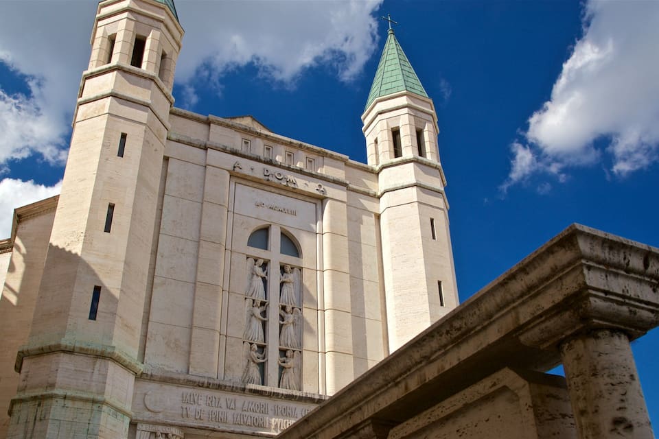 A historic church with two towers and a green spire, featuring detailed stone carvings and inscriptions.