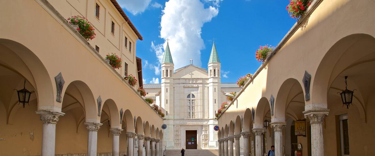 A historic building with two green spires, surrounded by arches and columns.