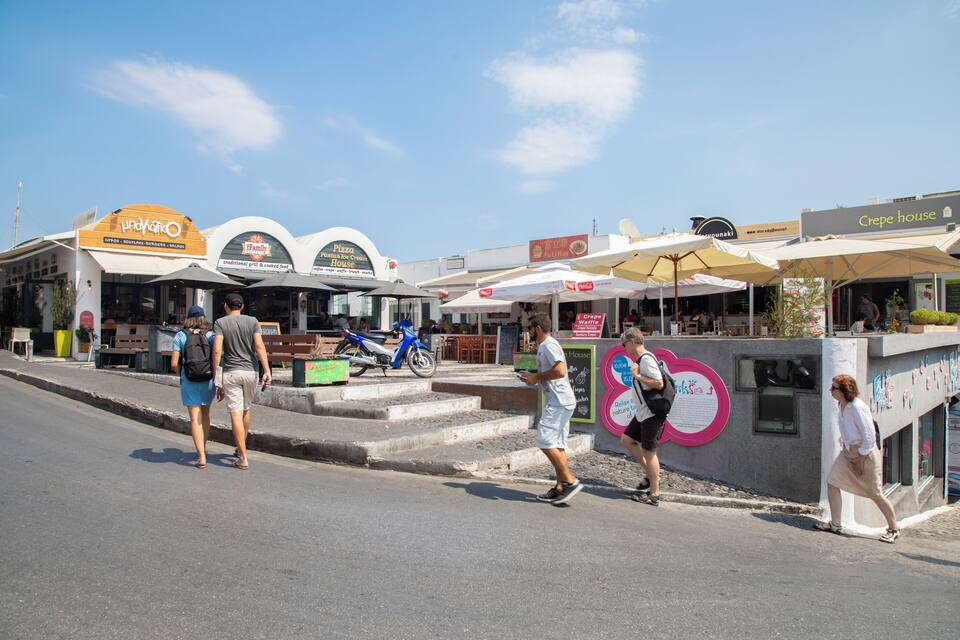 A street with people walking, a blue motorcycle parked, and various food and drink establishments.
