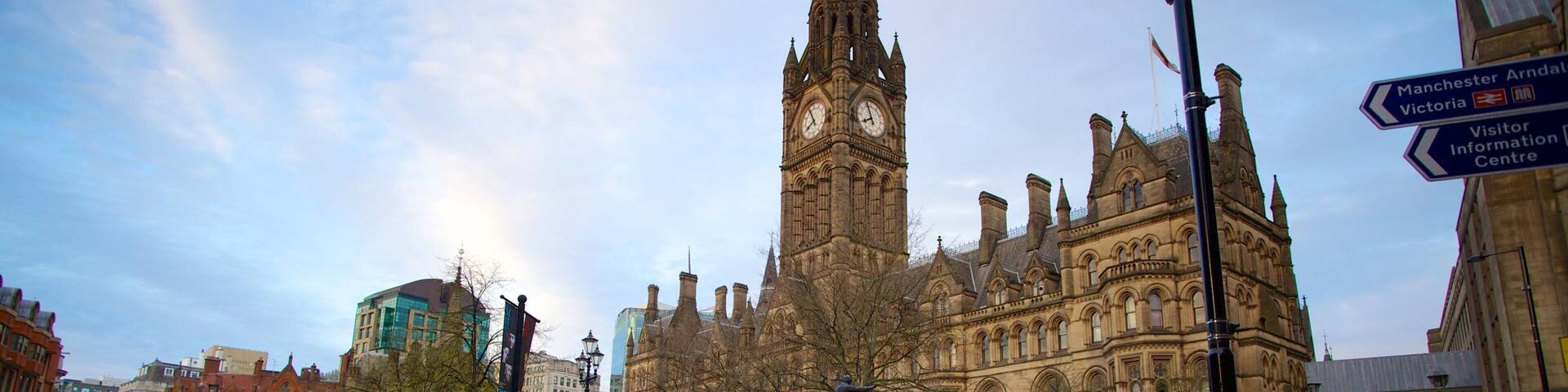 A historic building with a clock tower, surrounded by modern buildings and a busy street with cars and bicycles.
