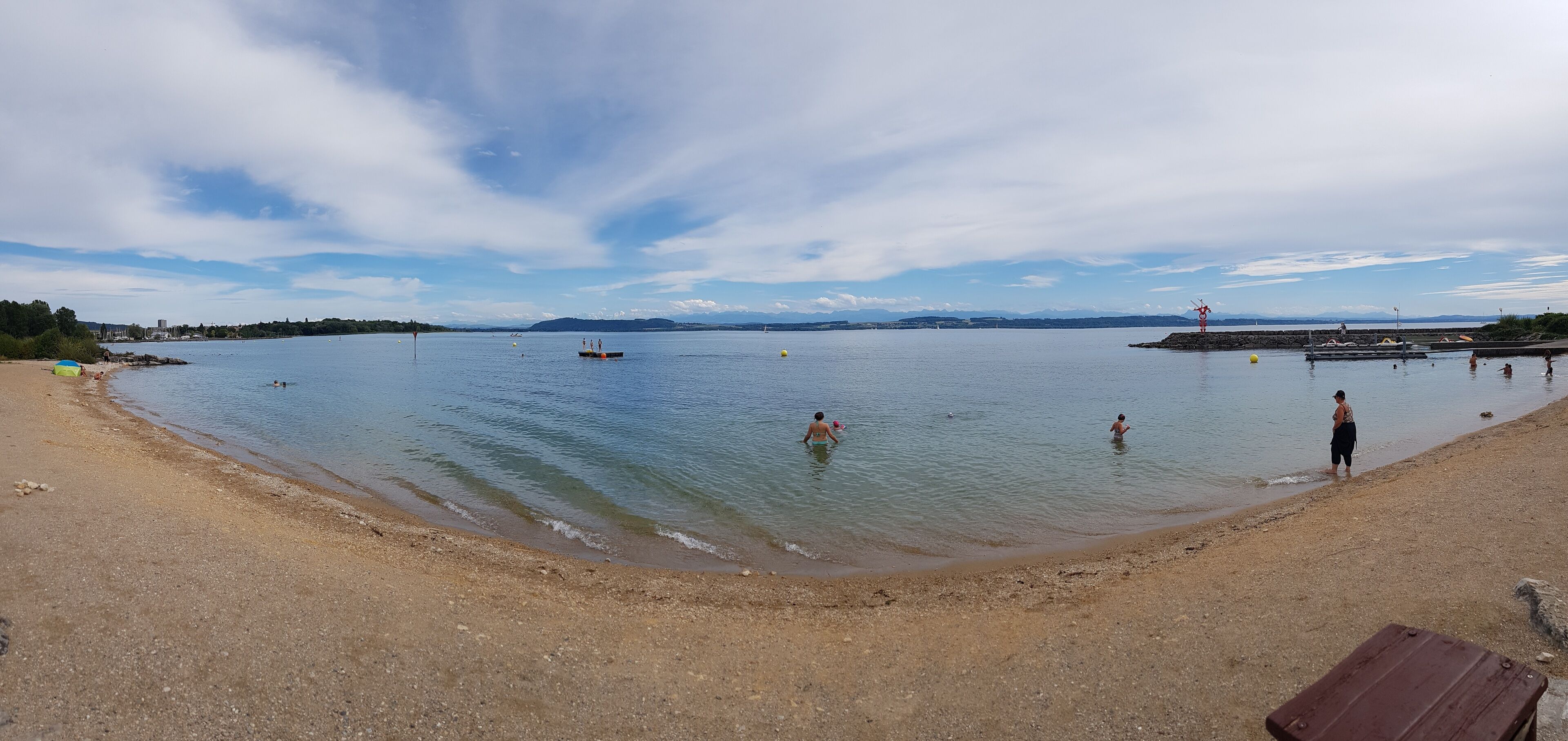 A beach with calm water, a few boats, and people swimming.