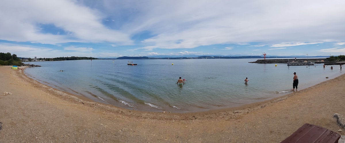 A beach with calm water, a few boats, and people swimming.