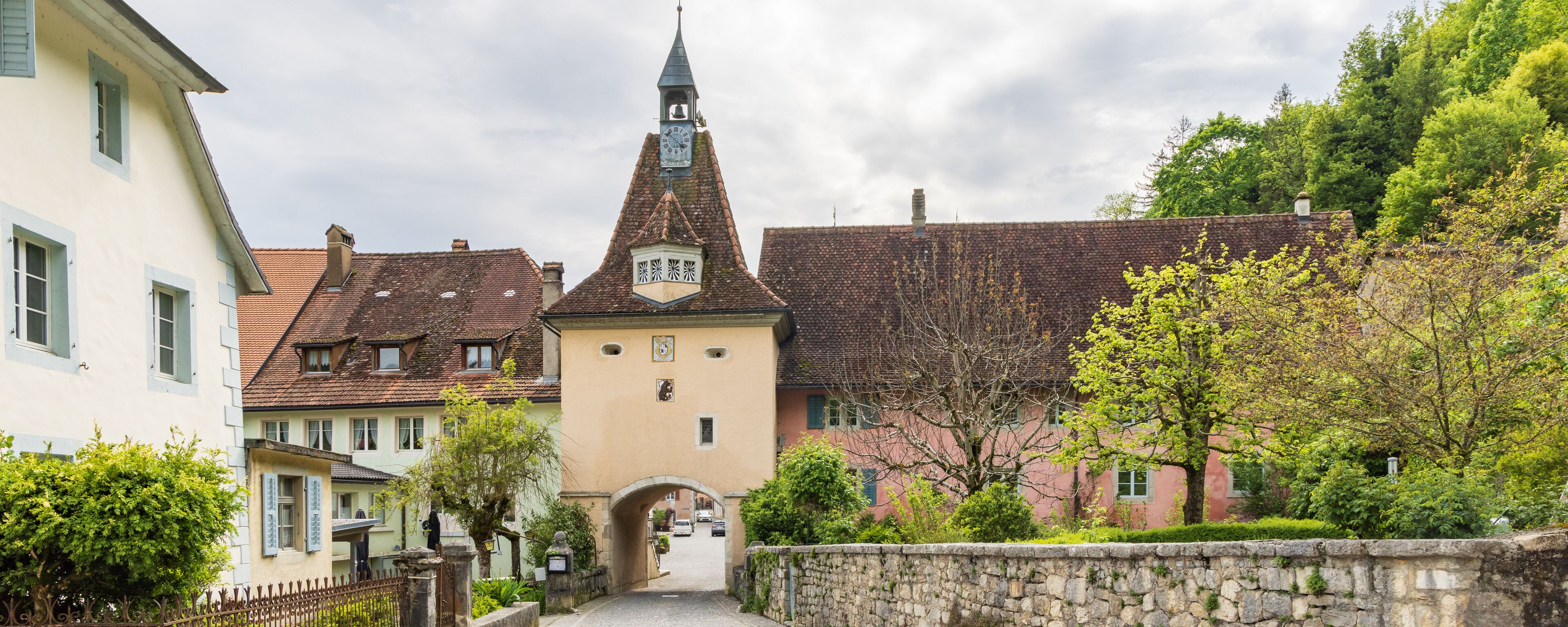 A quaint village with a prominent church tower, cobblestone streets, and lush greenery.