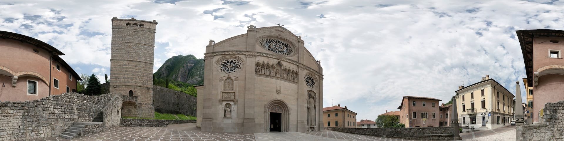 A historic plaza with a patterned pavement, a prominent church with a large circular window, and a stone tower.