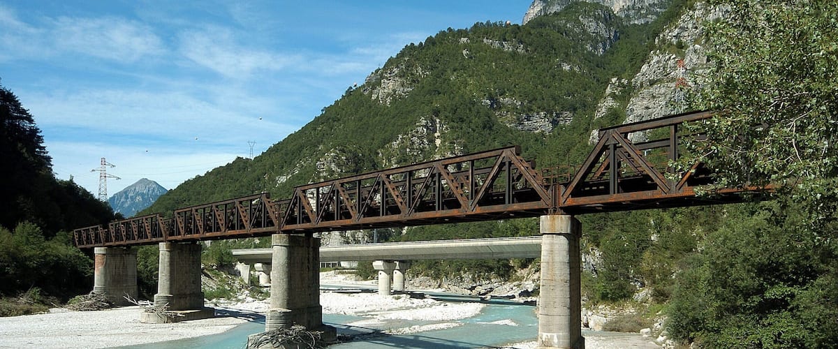 A steel bridge over a river with mountains in the background.