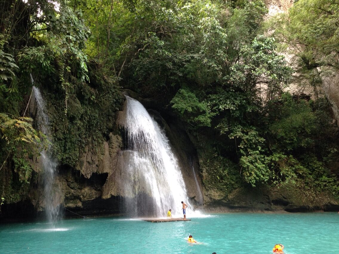 A waterfall cascading into a turquoise pool surrounded by lush greenery.