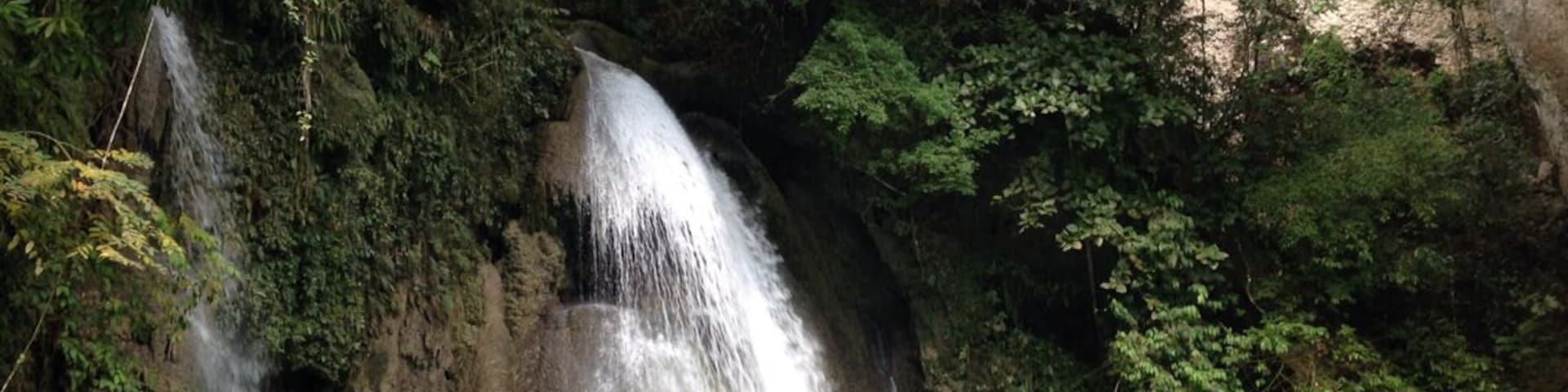 Uma cascata deságua em uma piscina azul-turquesa, cercada por vegetação exuberante.
