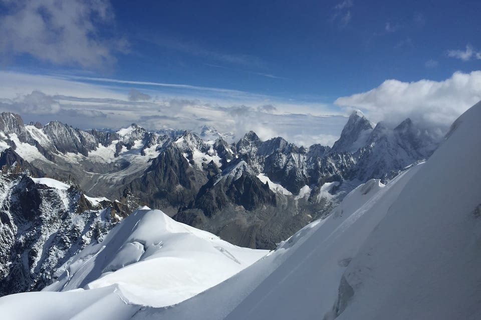 A snow-covered mountain range with sharp peaks and valleys under a clear blue sky.