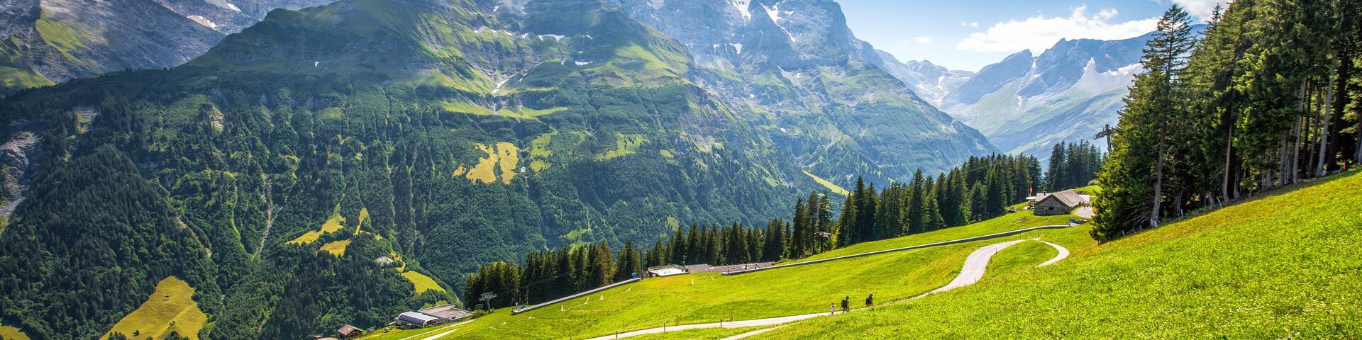 A mountainous landscape with a winding road, green fields, and a small building.