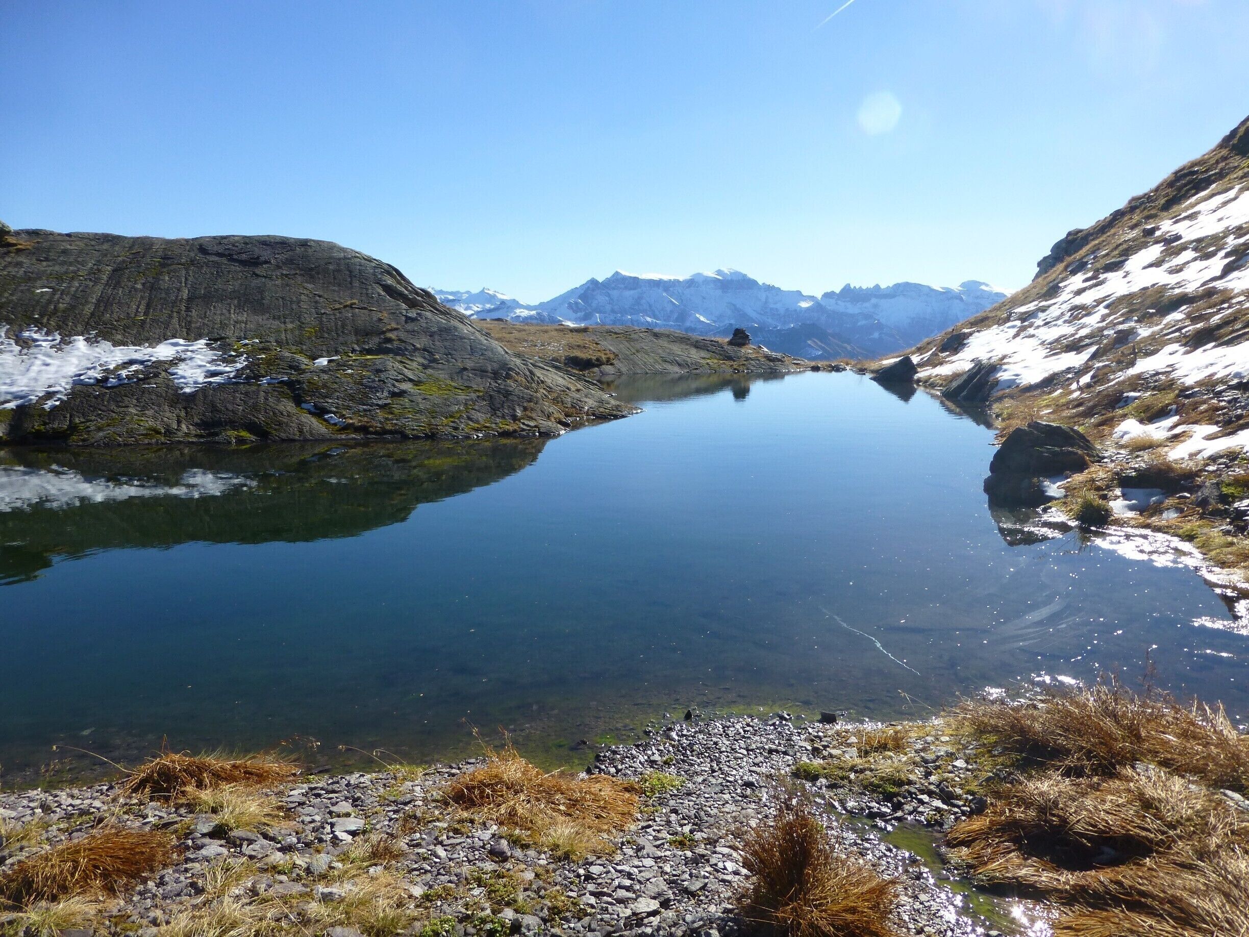 A clear mountain lake surrounded by rocky terrain and snow-capped peaks.