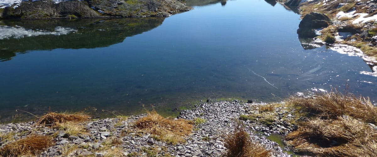 A clear mountain lake surrounded by rocky terrain and snow-capped peaks.