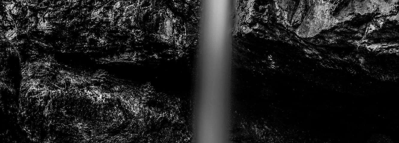 Una cascada que cae en una poza rodeada de terreno rocoso.