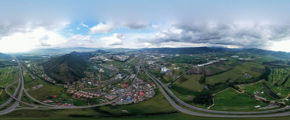 An aerial view of a town with winding roads, green fields, and a mountainous backdrop.