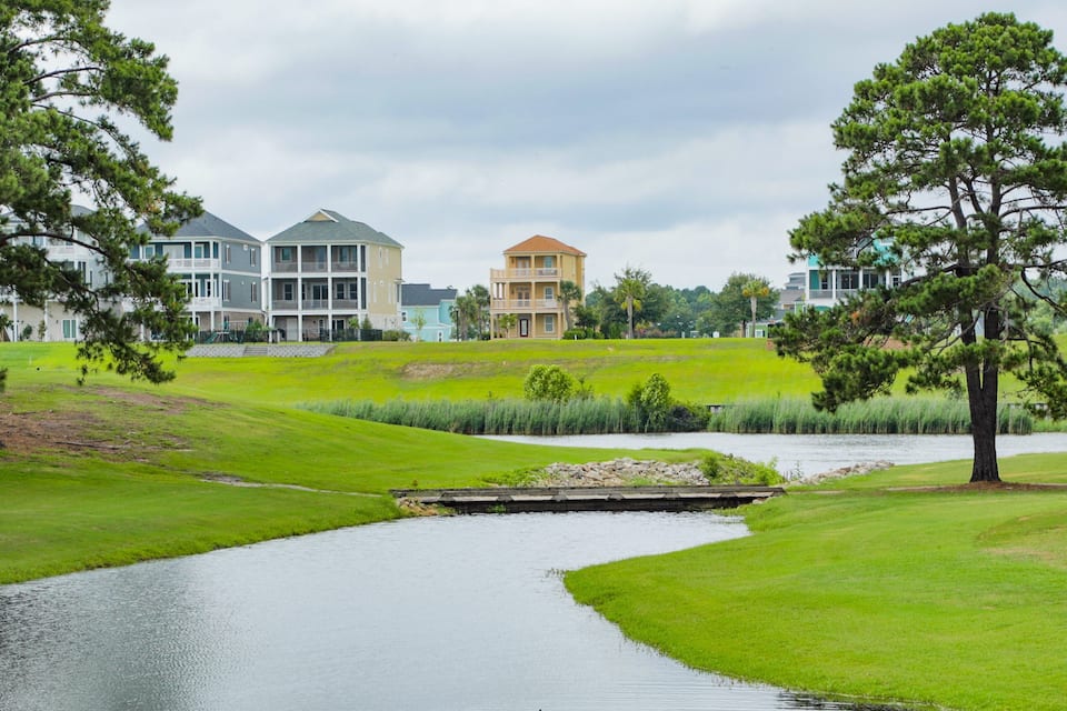Un campo de golf con un estanque, césped verde y edificios al fondo.