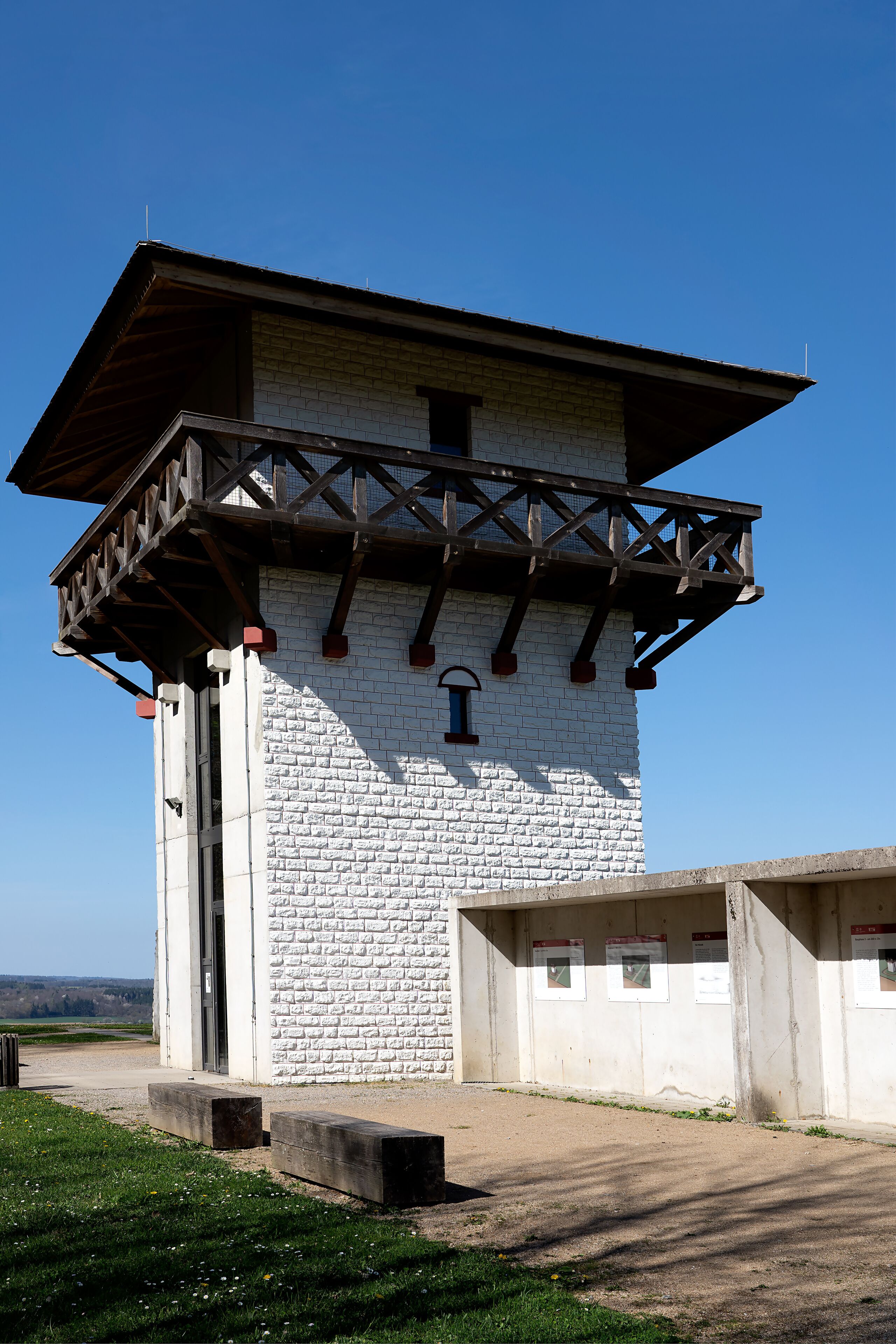 A white brick tower with a wooden balcony and a small window.