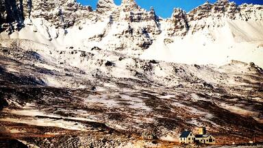 Una cadena montañosa nevada con una pequeña casa en primer plano.