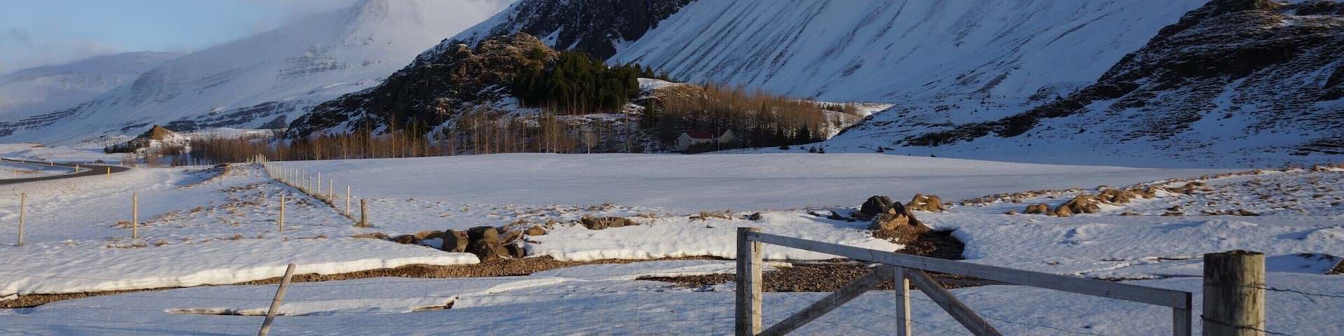 A snow-covered landscape with a wooden gate, mountains, and a clear sky.