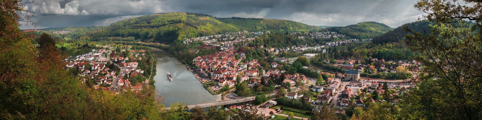 A town by a river with a bridge, surrounded by hills and greenery.