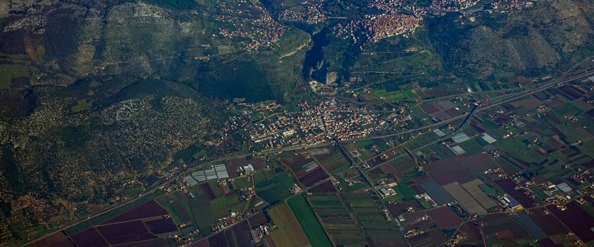 An aerial view of a town with a river, surrounded by fields and hills.