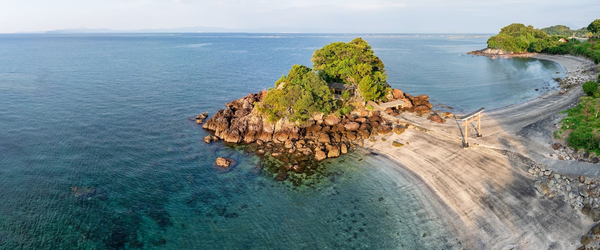 A coastal island with a clear blue sea, rocky shore, and a small building.